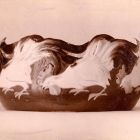 Photograph - Ornamental vessel with a row of pecking roosters emerging from a dark base, the wavy rim of the vessel follows the line of the roosters' tail feathers